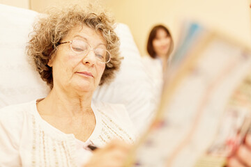 Senior woman reading a newspaper in bed at home