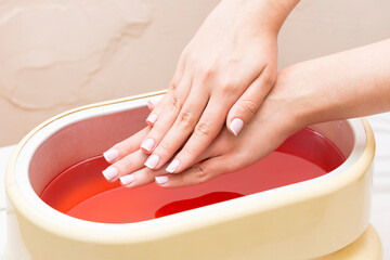 The process of paraffin therapy of a female hand is shot close up in a beauty salon. - obrazy, fototapety, plakaty