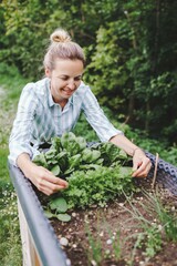 beautiful blond woman posing next to raised garden bed and her fresh vegetables