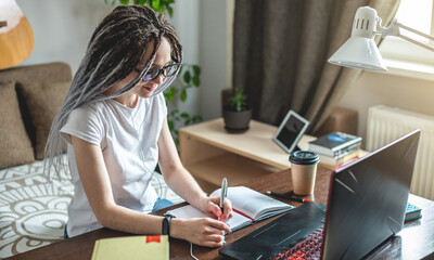 Beautiful girl student is studying at an online lesson at home on a laptop. Concept of distance education and exams