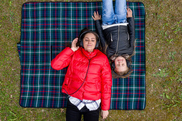 Obraz premium two sisters with closed eyes in headphones enjoys music lying on a checkered blanket in a forest