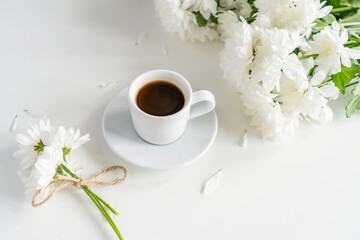 a coffee mug stands on a table on a white background, next to it are white chrysanthemums