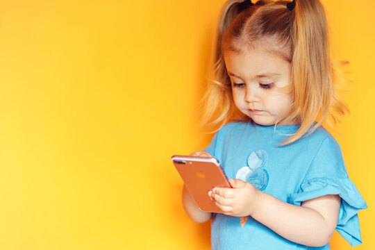  cute girl with ponytails uses a smartphone, smiling toddler, on an orange background, close-up, telephone conversation, telephone connection