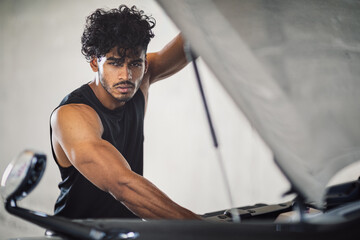 A handsome looking car mechanic repairman is opening the bonnet of the car and checking the engine