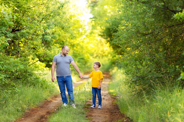 Fototapeta premium Happy young family: dad with son in casual wear, walk holding hands outdoors on a summer evening