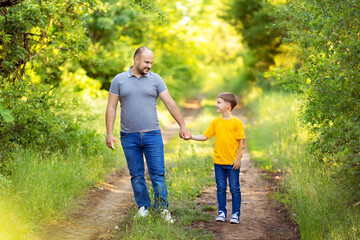 Fototapeta premium Happy young family: dad with son in casual wear, walk holding hands outdoors on a summer evening