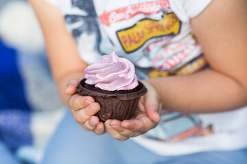 
A child in jeans clothes holds in his hands a chocolate cupcake with blueberry cream.