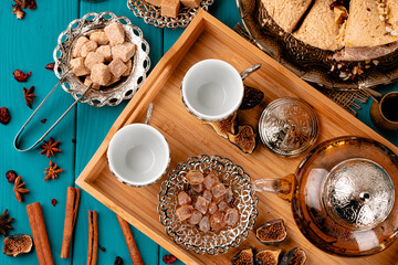 Fototapeta na wymiar Two empty cups on a wooden tray with sugar cubes and turkish baklava on blue wooden table decorated with cinnamon sticks