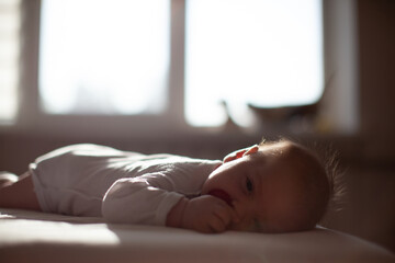 infant laying with pacifier on bed in lights of a sun