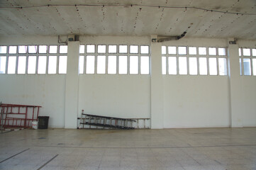 Interior de una nave industrial con paredes blancas y ventanales. 