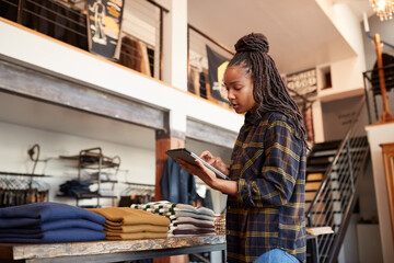 Female Owner Of Fashion Store Using Digital Tablet To Check Stock In Clothing Store