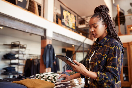 Female Owner Of Fashion Store Using Digital Tablet To Check Stock In Clothing Store