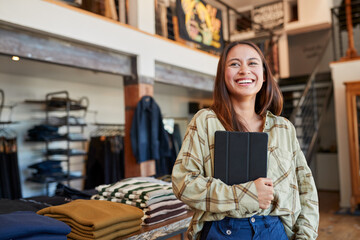 Portrait Of Female Owner Of Fashion Store Using Digital Tablet To Check Stock In Clothing Store - Powered by Adobe