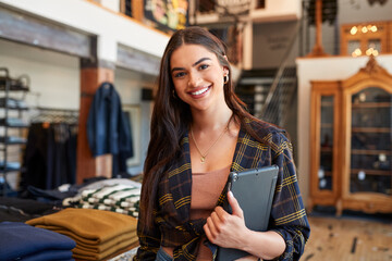 Portrait Of Smiling Female Owner Of Fashion Store Standing In Front Of Clothing Display