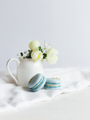Fototapeta na wymiar Tasty blue french macarons and jar with cream roses on a white wooden background.