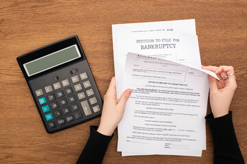 cropped view of woman with bankruptcy papers near calculator on wooden background