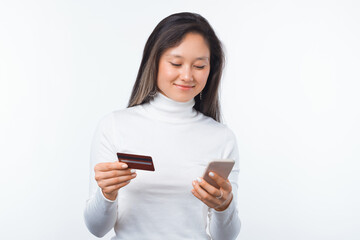 Naklejka premium Smiling woman is using mobile banking while holding a phone and a card on white background