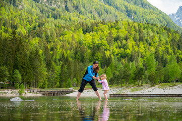Fototapeta na wymiar Mother and daughter walking across forest lake.