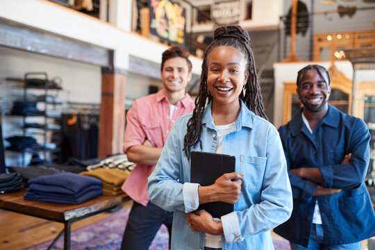 Portrait Of Smiling Multi-Cultural Sales Team In Fashion Store In Front Of Clothing Display