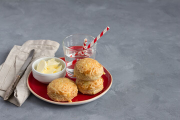 Homemade freshly baked scones with cheese and herbs on a red plate with butter on a gray textured...