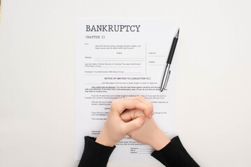 cropped view of female clenched hands on bankruptcy paper near pen on white background