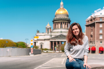 Fototapeta premium Portrait of a girl with long hair in a sweater on a Sunny summer day against the background of St. Petersburg street, with St. Isaac's Cathedral