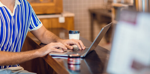 Young man drinking coffee in cafe and using laptop computer. Freelancer working from coffee shop