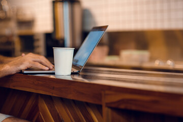 Close up of man's hands, coffee cup and laptop computer. Freelancer working from coffee shop