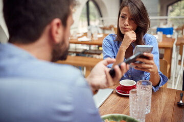 caucasian couple talking in a restaurant with cell phones in their hands.
