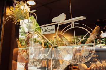 Decorative bicycle with flowers, pastry and card with welcome lettering on showcase of bakery