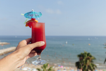 Cropped view of man holding glass of cocktail with seascape and blue sky at background