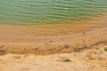 Fototapeta na wymiar Small waves on greenish water and a sandy beach. Beautiful pond on a sand quarry 