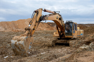 Fototapeta na wymiar Excavator working at construction site. Backhoe digs ground for the foundation and for paving out sewer line. Construction machinery for excavating, loading, lifting and hauling of cargo on job sites