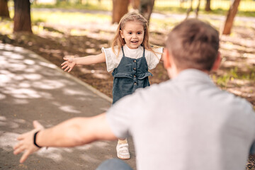  dad with little daughter play in the park on the street, toddler runs to meet dad, child hugs dad, close-up, concept happy father's day.