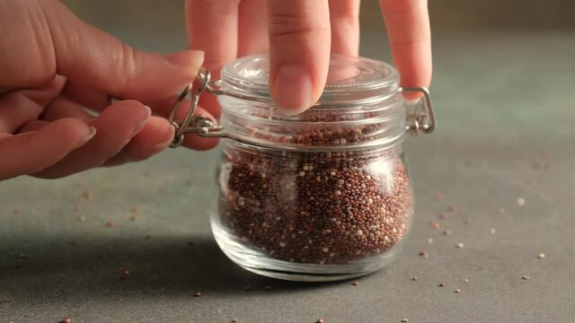 Red raw quinoa, South American grain, female hands close glass jar. Healthy and gluten free food.