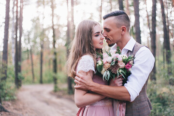 Beautiful couple at the photoshoot of love story in the forest in a rustic dress