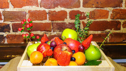 Set of berries and fruits in wooden box. Apple, strawberry, grape, berry and peach on a red brick...