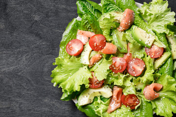 Salmon salad with avocado, green leaves tomatoes on dark background.
