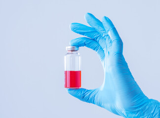 Medical theme: doctor's hand in a blue glove holding a vial of liquid for injection. The scientist's hand holds a vial of vaccine.