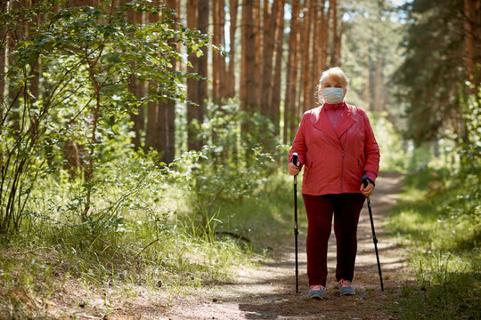 a woman in a protective mask walks in a Park with sticks for Nordic walking, a walk in the fresh air after quarantine, a precautionary measure against the virus