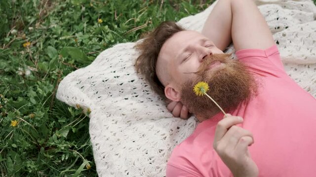 man with dandelion lying in meadow on grass, sneezing from allergies to flowers, Sunny summer weather,man with beard and mustache in pink t-shirt,concept of health