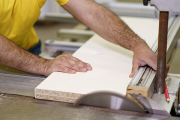 Carpenter hands cutting a piece of wood for furniture in his woodwork workshop, using a table saw.