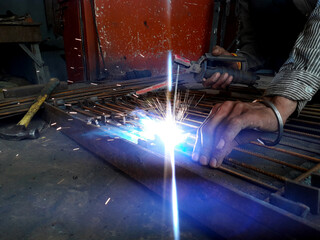 Fototapeta na wymiar Generating blue sparks while worker welding on iron in industrial workshop