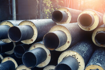 Heap of many new black insulated steel pipes at municipal construction site outdoors. Heating main...