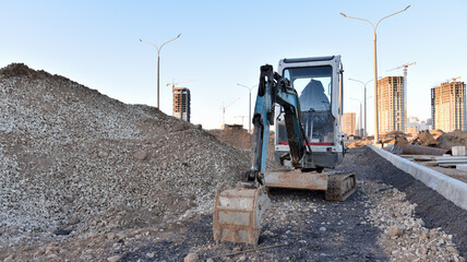 Mini excavator digg trench to lay cables concrete curbs and paving slabs at construction site....