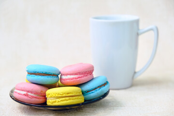 Colorful french Sweet Cakes Macaroons on a glass plate and white coffee mug.
