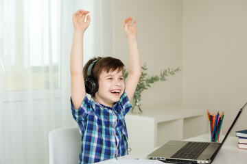 Naklejka premium boy with headphones raised his hands and laughs, working on the computer at home