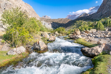 The beautiful mountain trekking road with clear blue sky and rocky hills and fresh mountain stream in Fann mountains in Tajikistan