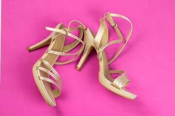 Women's beige sandals with rhinestones on high heels, on a pink background. Women's shoes. Lying sideways