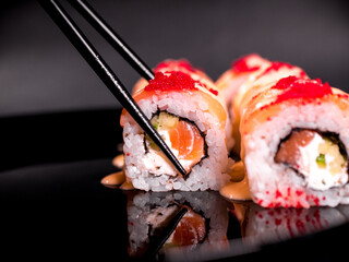 hand holding a roll of chopsticks over sushi roll on a dark background